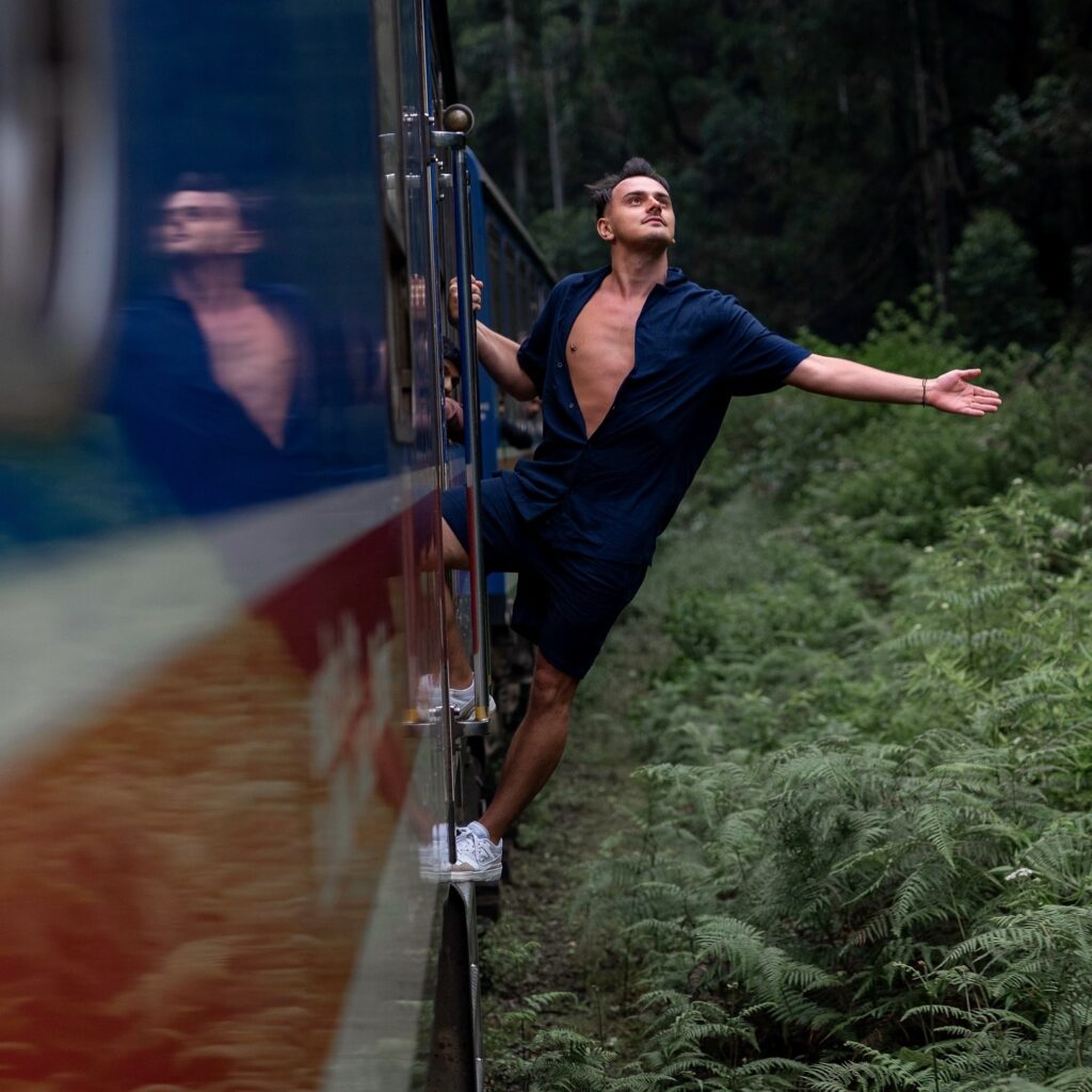 Man hangs of the side of a train, enjoying the scenery.